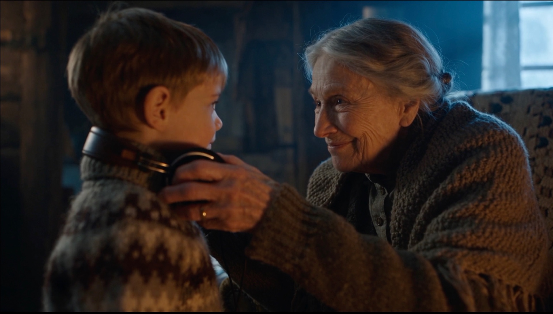 A grandmother placing headphones over a young boy's ears in a warm cabin